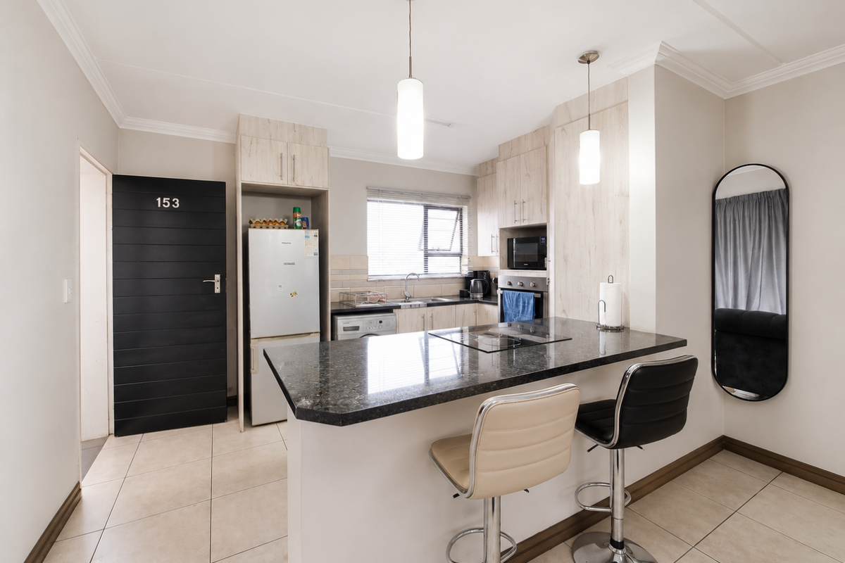 Modern kitchen featuring granite countertops, built-in appliances, laminate cabinetry, and a breakfast bar with pendant lighting, finished with neutral tiled flooring.