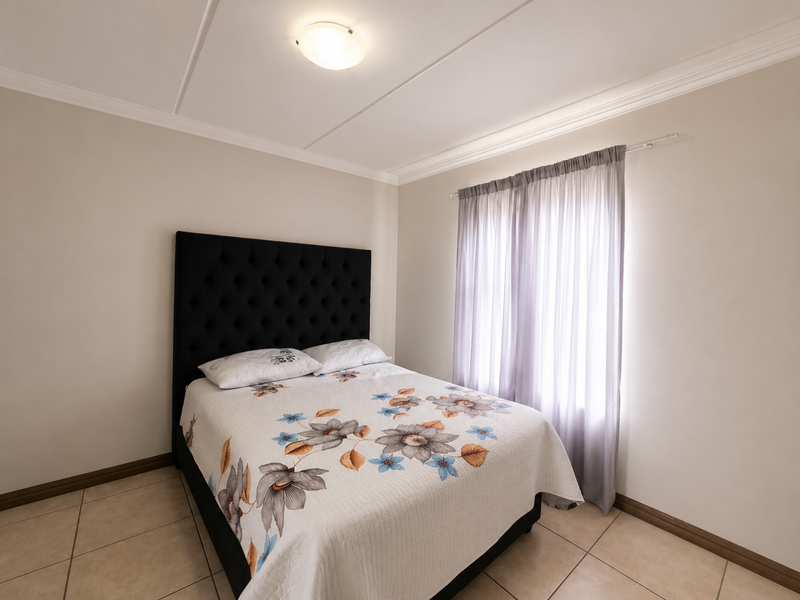 A well-maintained bedroom featuring neutral wall tones, tiled flooring, and classic ceiling cornicing, providing a clean and functional living space.