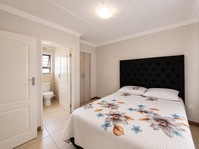 A well-maintained bedroom featuring tiled flooring, built-in wardrobe storage, and an adjoining en-suite bathroom with a toilet.
