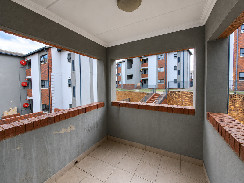 A covered balcony featuring tiled flooring and a brick-topped parapet wall, offering views of the surrounding apartment complex.