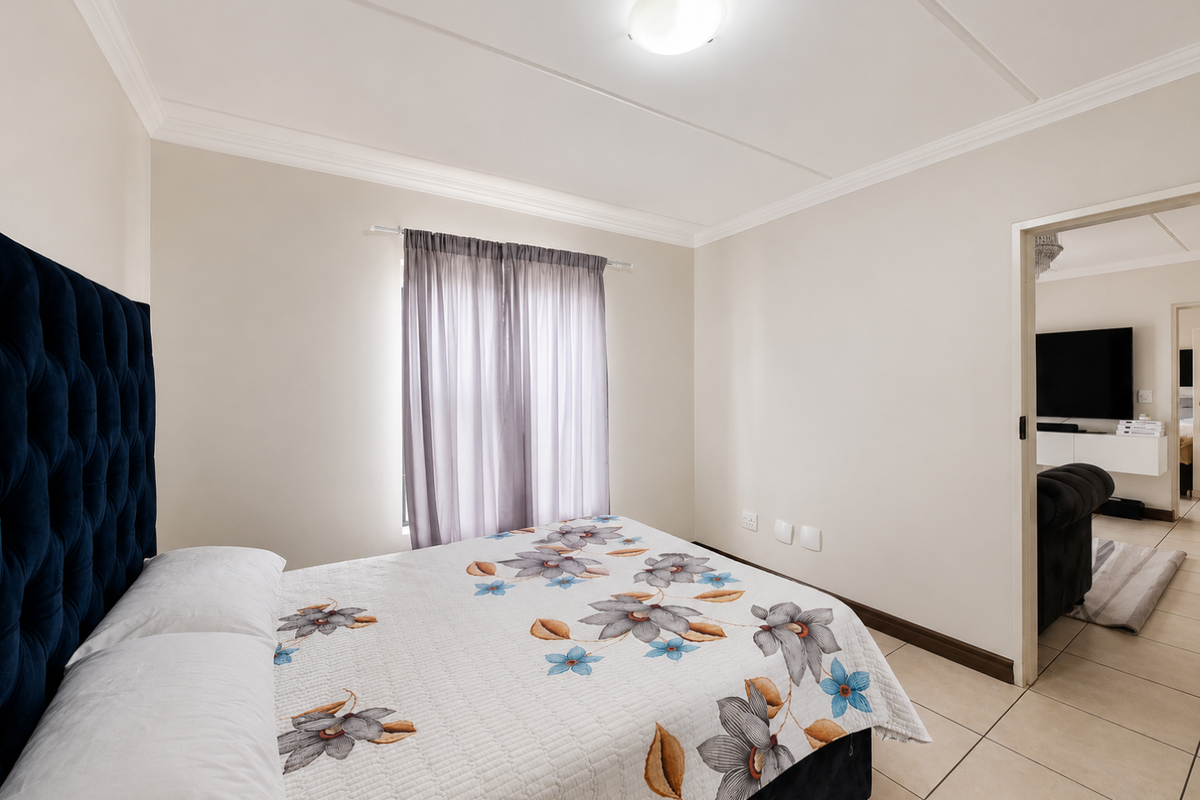 A well-maintained bedroom featuring neutral walls, tiled flooring, and a ceiling light, with a view into the adjacent living area.
