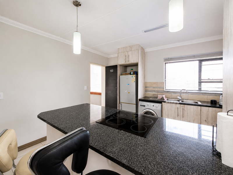 Modern kitchen featuring granite countertops, an integrated electric hob, built-in cabinetry, and a stainless steel sink with a tiled backsplash.