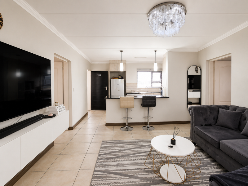 A well-maintained open-plan living and kitchen area featuring tiled floors, a central kitchen island, and modern built-in cabinetry with elegant lighting fixtures.