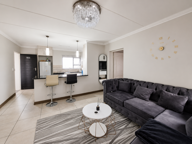A well-maintained open-plan living and kitchen area featuring tiled floors, modern cabinetry, granite countertops, and an elegant crystal chandelier.