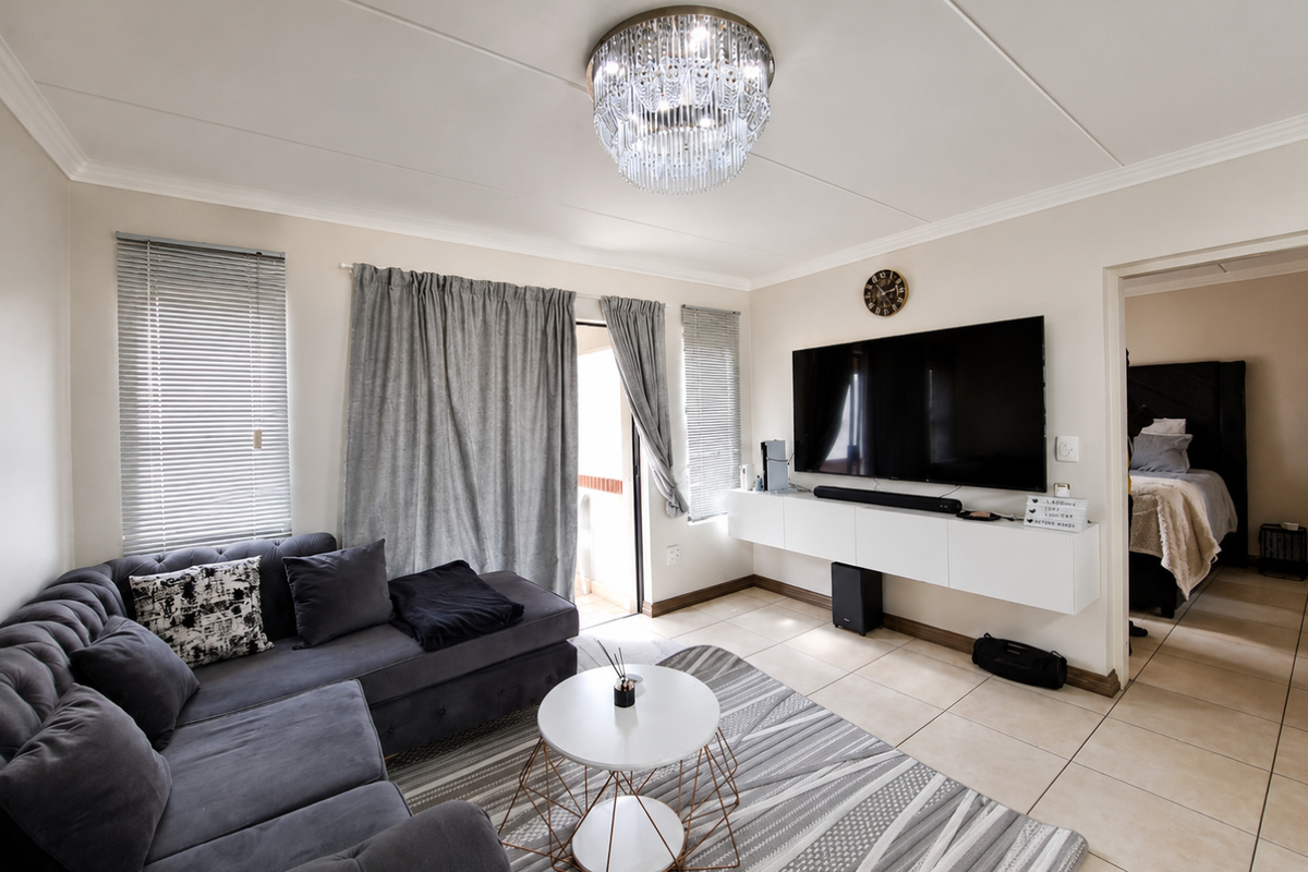 A well-maintained living room featuring tiled floors, a wall-mounted media console, and a crystal chandelier, with direct access to a balcony.