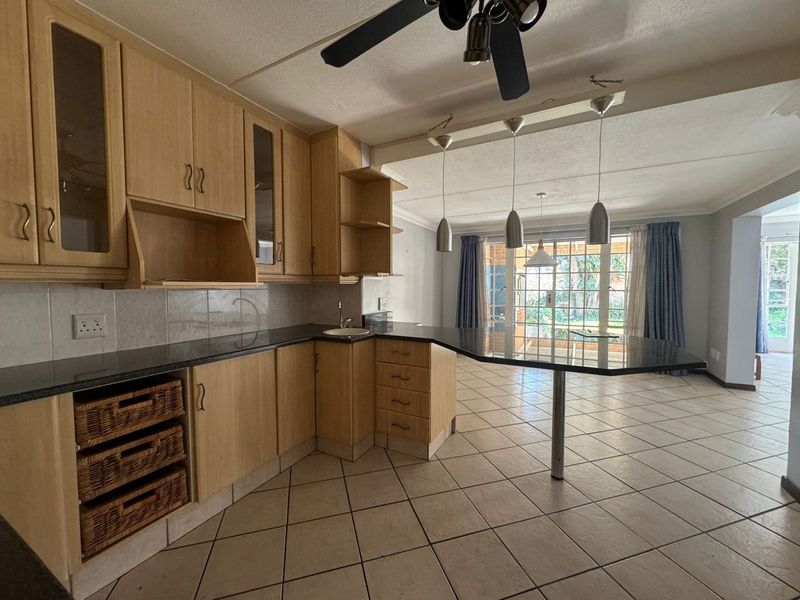 Open-plan kitchen and living area featuring light wood cabinetry, granite countertops, a breakfast bar, and ceramic tiled flooring with direct access to the garden.
