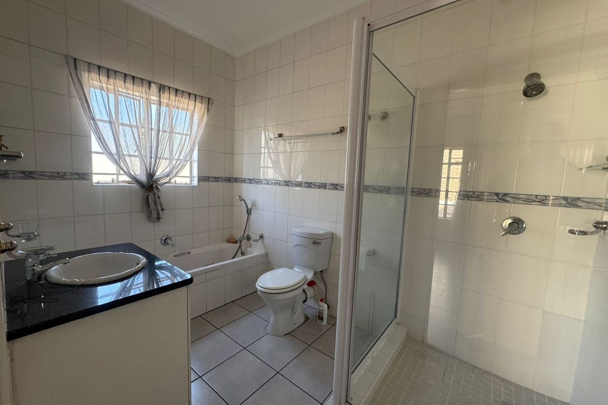 A functional bathroom featuring a vanity with granite countertop, a built-in bathtub, a separate shower enclosure, and tiled finishes throughout.