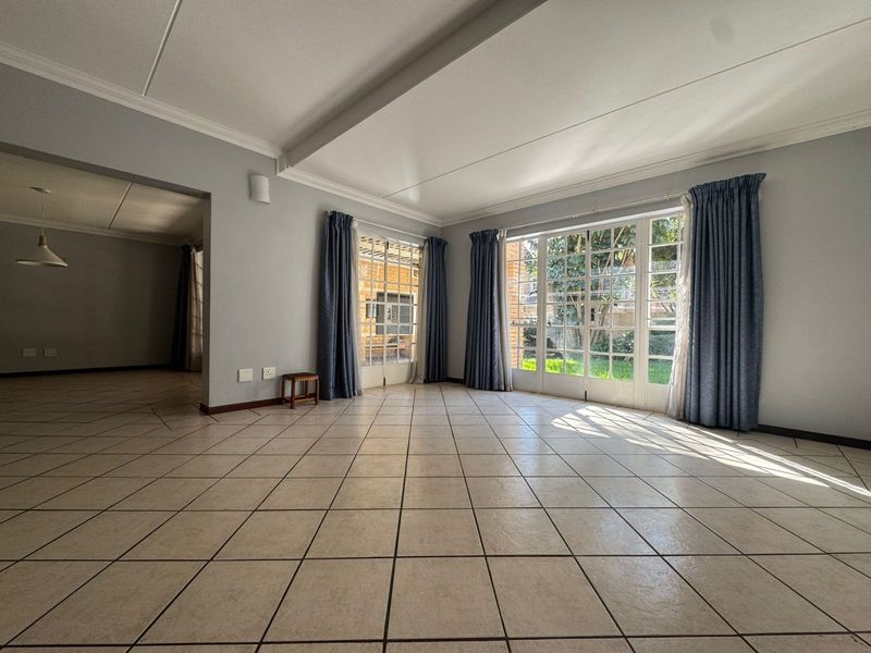 Spacious, light-filled living area featuring neutral ceramic floor tiles, elegant cove cornicing, and large french doors providing direct access to the garden.