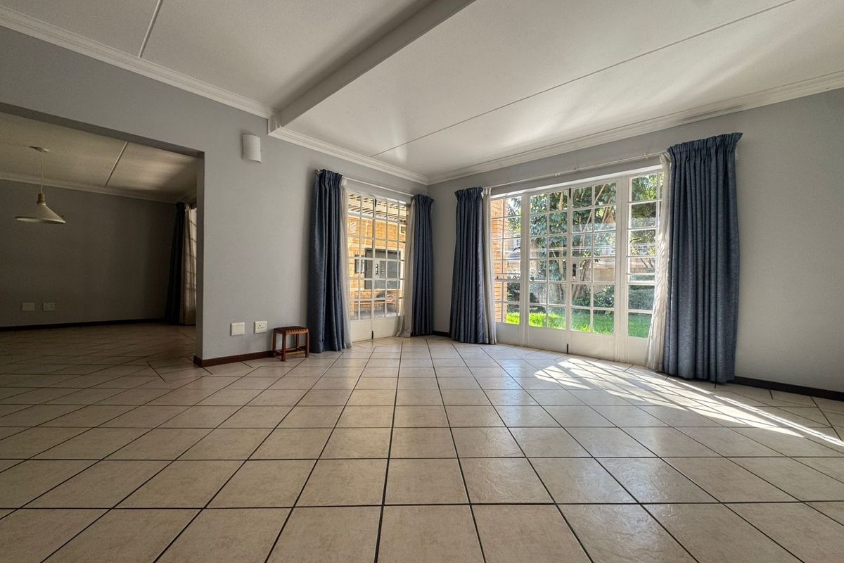 Spacious, light-filled living area featuring neutral ceramic floor tiles, elegant cove cornicing, and large french doors providing direct access to the garden.
