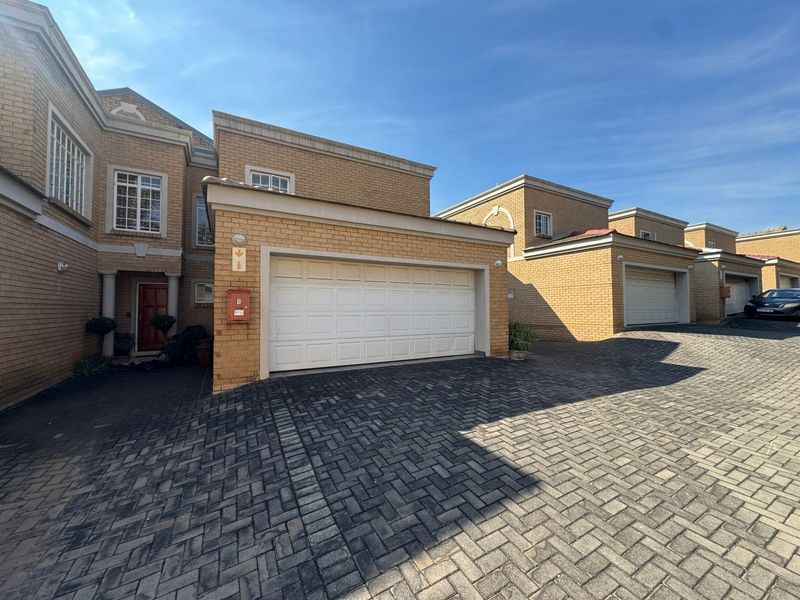 Front elevation of a townhouse complex featuring a brick facade, paved driveway, and double garage door access.