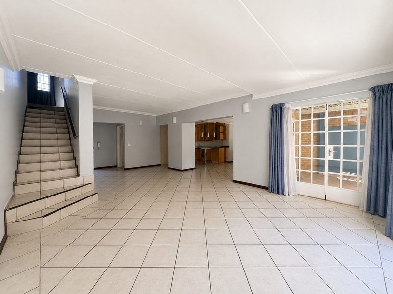 Spacious open-plan living area featuring tiled flooring, a central staircase, and direct access to an outdoor patio through glass-paned french doors.