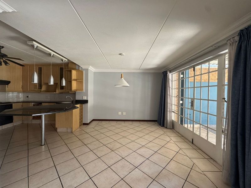 Spacious open-plan living and kitchen area featuring tiled flooring, wooden cabinetry, granite countertops, and large glass french doors leading to an outdoor space.
