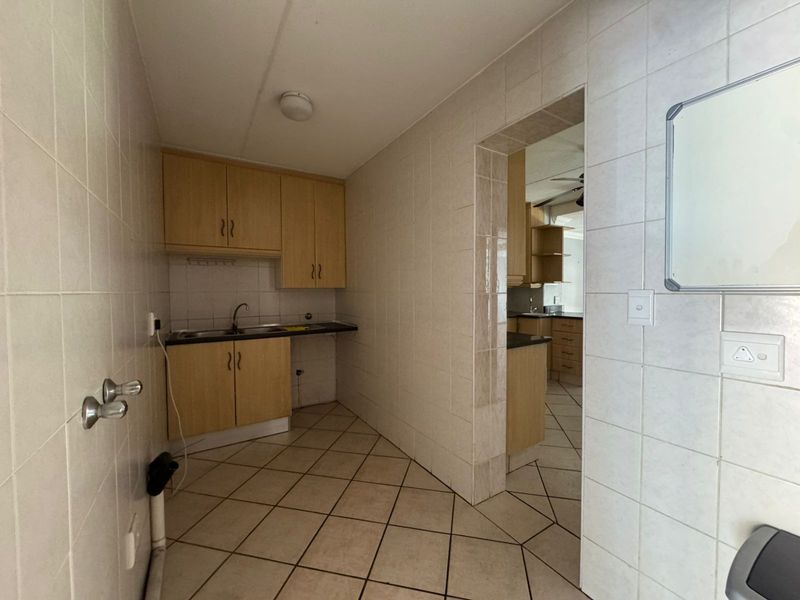 A functional scullery area featuring tiled walls, built-in cabinetry, and a stainless steel sink, providing additional prep and wash-up space.