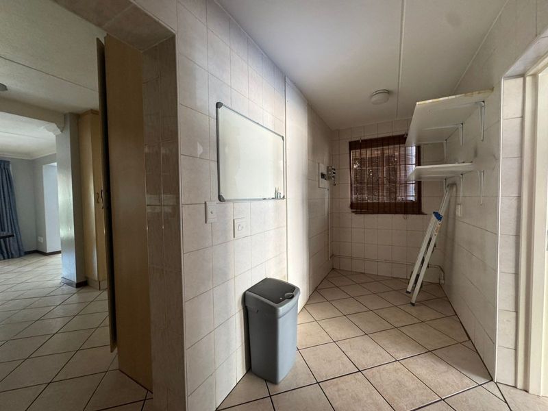 A functional laundry or utility space featuring full-height wall tiling, ceramic floor tiles, and built-in shelving units.