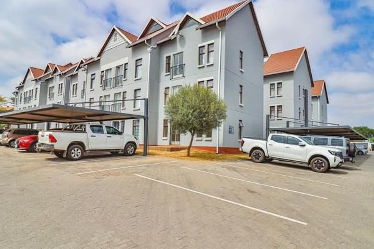 Exterior view of a multi-story apartment complex featuring paved parking bays and covered carport structures.