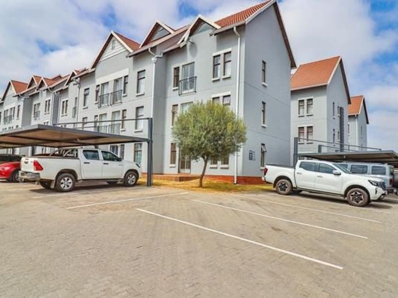 Exterior view of a multi-story apartment complex featuring paved parking bays and covered carport structures.