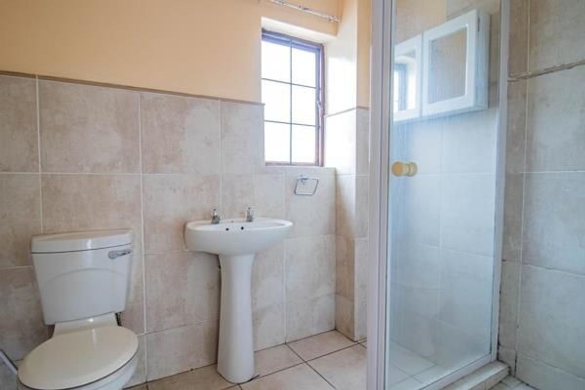 A functional bathroom featuring a pedestal basin, toilet, and a glass-enclosed shower with neutral wall and floor tiling.
