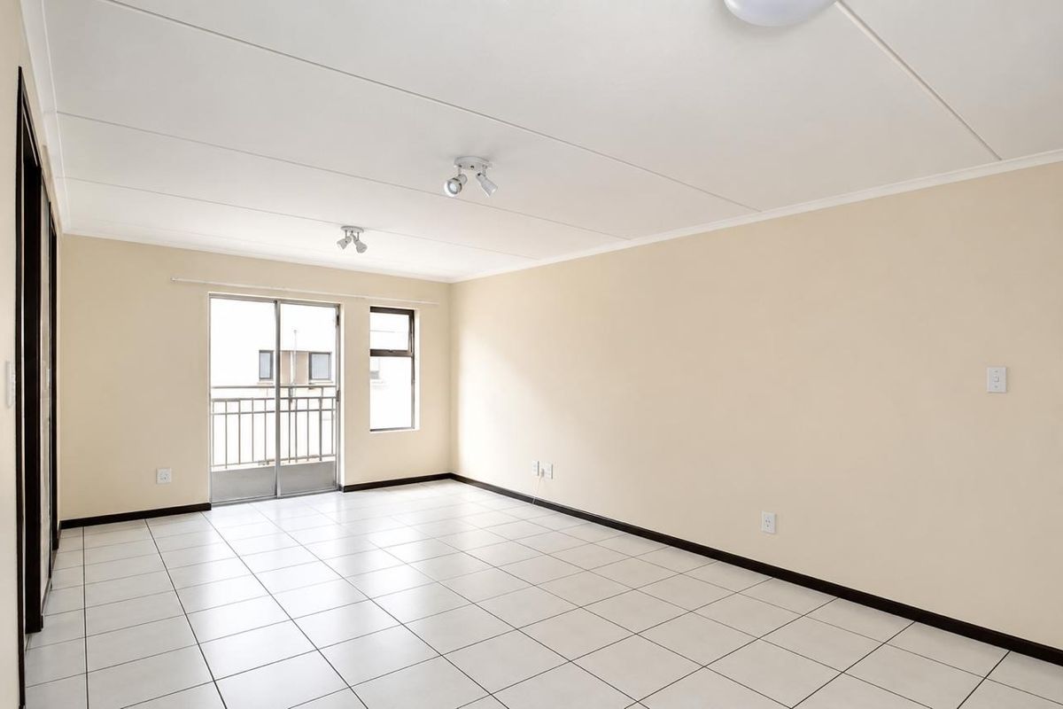 Spacious, empty living area featuring neutral tiled flooring, clean walls, and a sliding glass door providing access to a balcony.