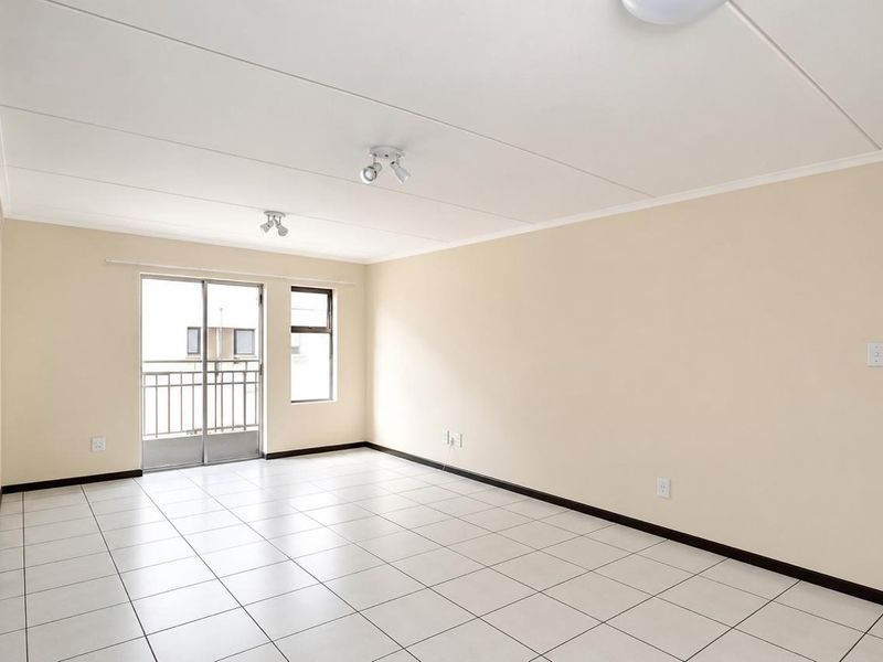 Spacious, empty living area featuring neutral tiled flooring, clean walls, and a sliding glass door providing access to a balcony.