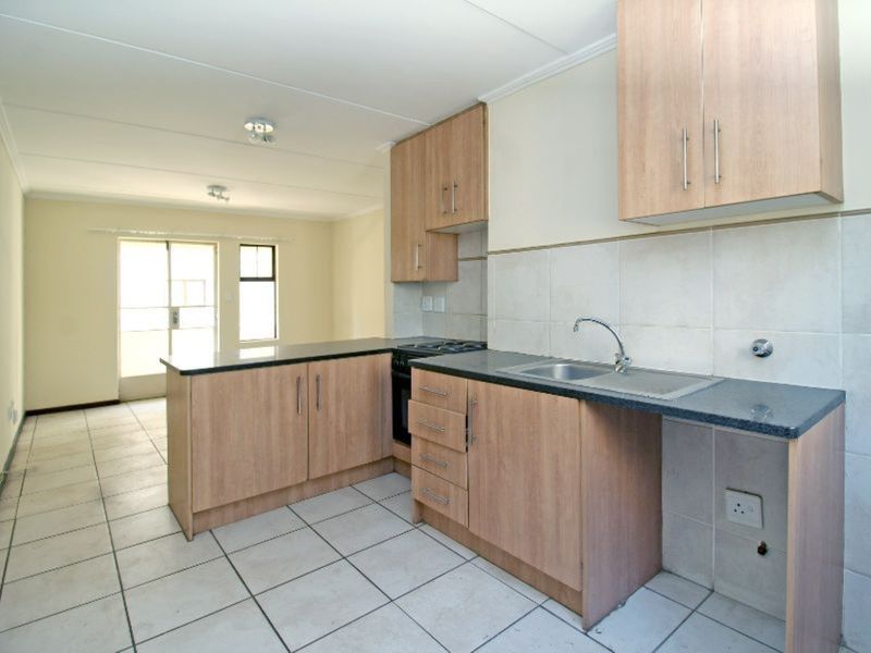 Open-plan kitchen and living area featuring light wood cabinetry, dark countertops, tiled flooring, and direct access to an outdoor space via a sliding door.
