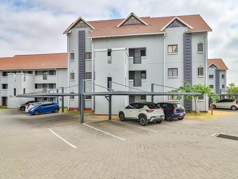 Exterior view of a multi-story apartment complex featuring a paved parking area with covered carports and tiled roofing.