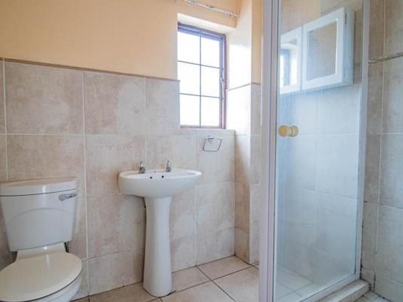 A functional bathroom featuring a pedestal basin, toilet, and a glass-enclosed shower with neutral wall and floor tiling.