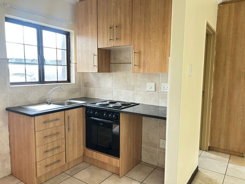 Compact kitchen featuring light wood-finish cabinetry, dark laminate countertops, built-in oven and hob, and neutral tiled backsplash and flooring.