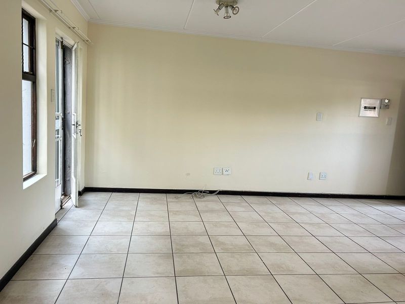 An empty living room featuring neutral tiled flooring, a glass panel door leading outside, and a large blank wall ready for personalization.
