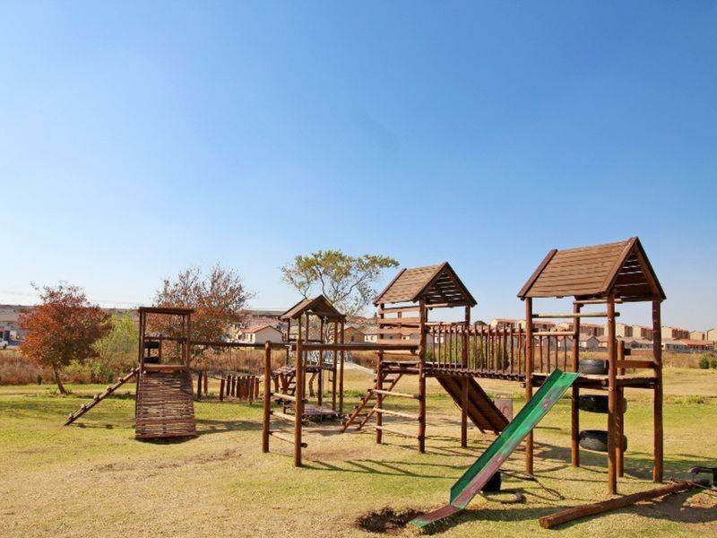 Outdoor communal garden area featuring a wooden playground structure with a slide and climbing equipment set within a landscaped residential complex.