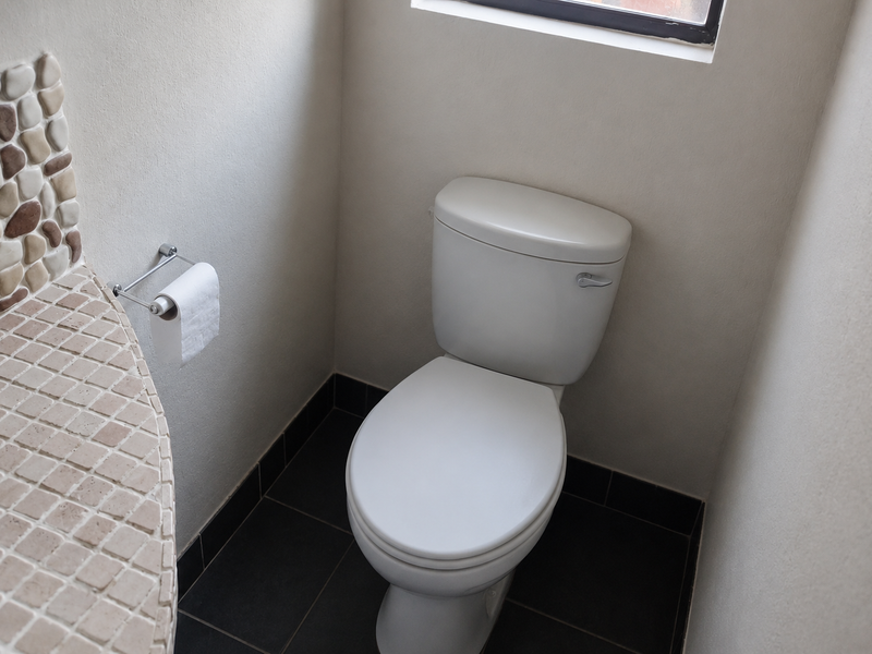 A compact bathroom featuring a white toilet, tiled vanity surface with decorative stone accents, and dark floor tiles.