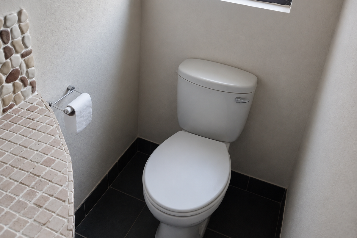 A compact bathroom featuring a white toilet, tiled vanity surface with decorative stone accents, and dark floor tiles.