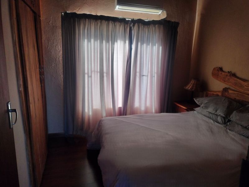 A cozy bedroom featuring built-in wooden cabinetry, laminate flooring, and an integrated air conditioning unit, providing a functional and comfortable living space.