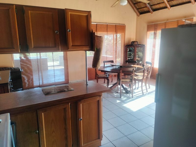 Open plan kitchen and dining area featuring wooden cabinetry, tiled flooring, and a traditional thatch ceiling with a ceiling fan.