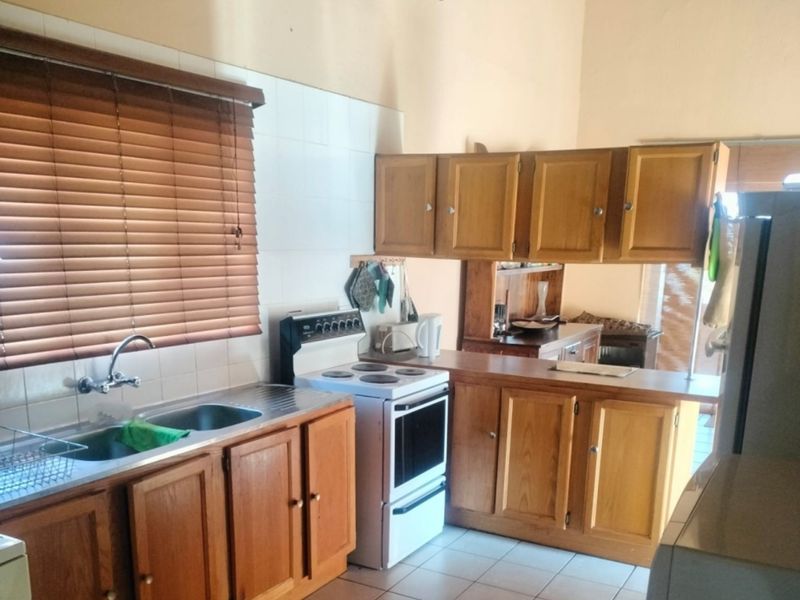 A functional kitchen featuring wooden cabinetry, a double bowl stainless steel sink, a freestanding electric stove, and tiled splashbacks with neutral floor tiles.