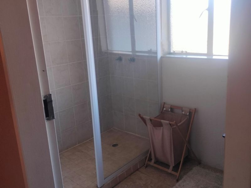 A functional bathroom featuring a tiled shower enclosure and a window, presenting an opportunity for modernization and cosmetic updates.