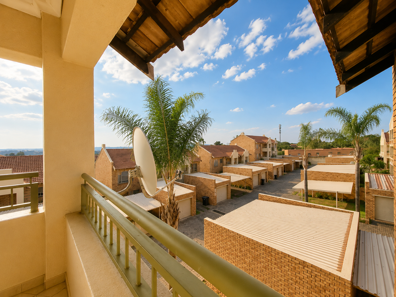 A covered balcony with tiled flooring and metal railings, offering an elevated view over the townhouse complex and surrounding neighborhood.