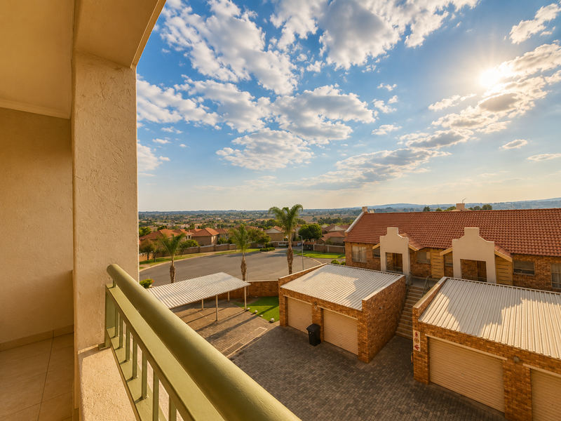 A view from a balcony overlooking a residential townhouse complex with brick garages and paved driveways under a clear sky.