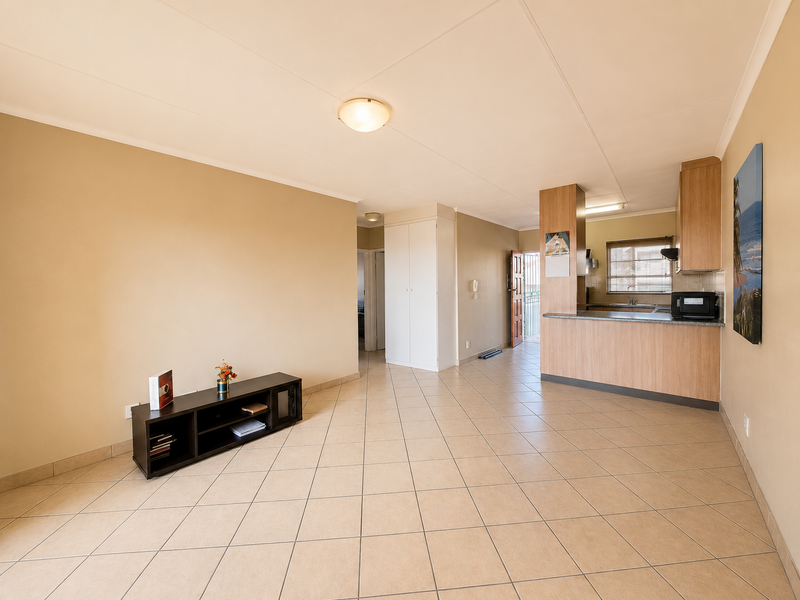 Open-plan living area featuring tiled flooring, a functional kitchen with breakfast bar, and built-in storage cupboards.