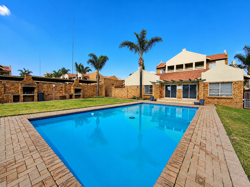 A well-maintained communal pool area featuring brick paving, built-in braai facilities, and direct access to the townhouse units.