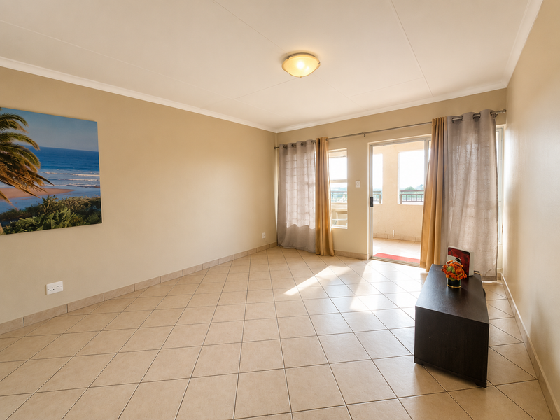 A bright and spacious living area featuring neutral tiled flooring and a sliding glass door that opens onto a private balcony.