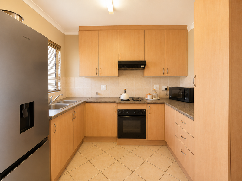A functional U-shaped kitchen featuring light wood cabinetry, laminate countertops, built-in oven, electric hob, and tiled flooring.