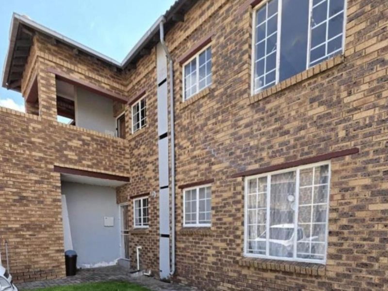 Exterior view of a multi-story face brick apartment building featuring multiple windows, a balcony, and functional guttering systems.
