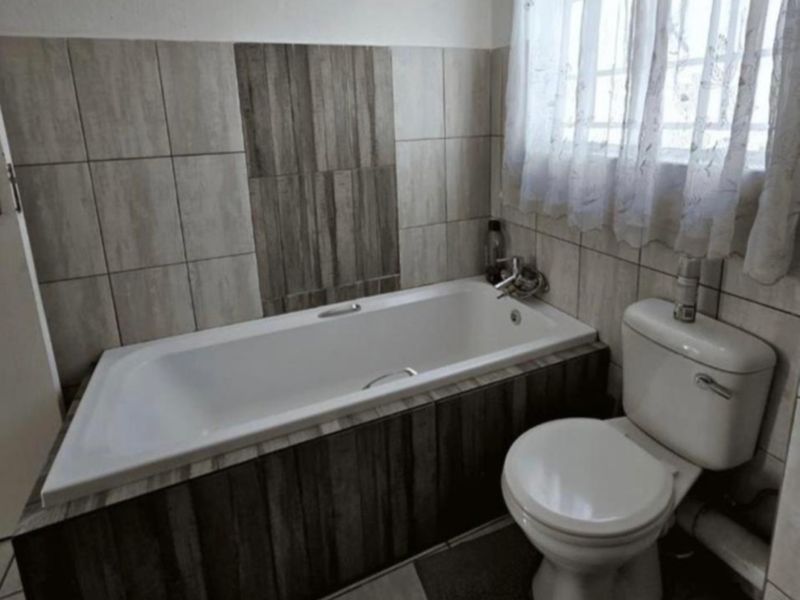 A functional bathroom featuring a built-in bathtub with wood-look tile surround, a standard toilet, and neutral wall tiling.