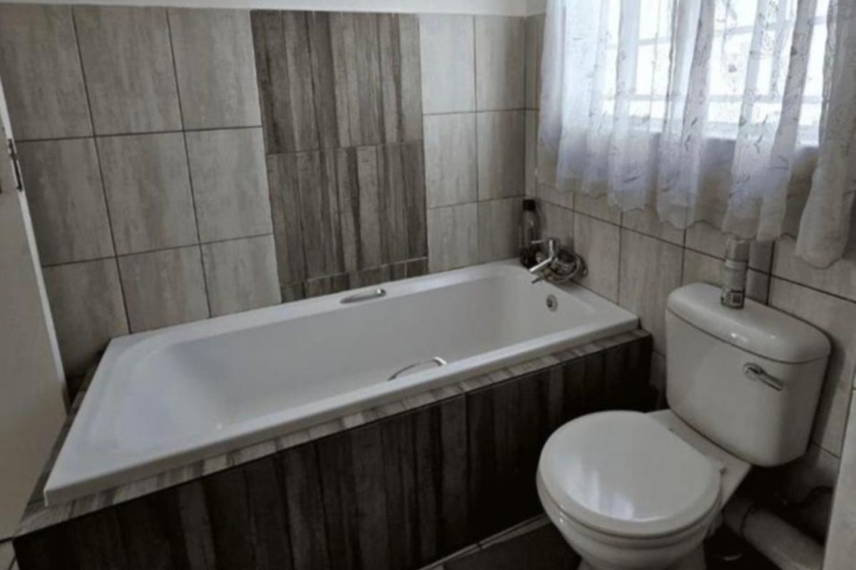 A functional bathroom featuring a built-in bathtub with wood-look tile surround, a standard toilet, and neutral wall tiling.
