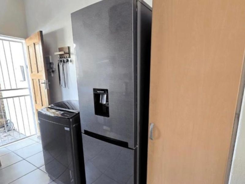 A functional laundry area featuring tiled flooring, a built-in storage cupboard, and direct access to an exterior security gate.