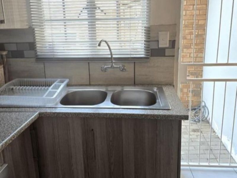 A functional kitchen area featuring a double bowl stainless steel sink, laminate cabinetry, and a tiled backsplash with direct access to an outdoor area.