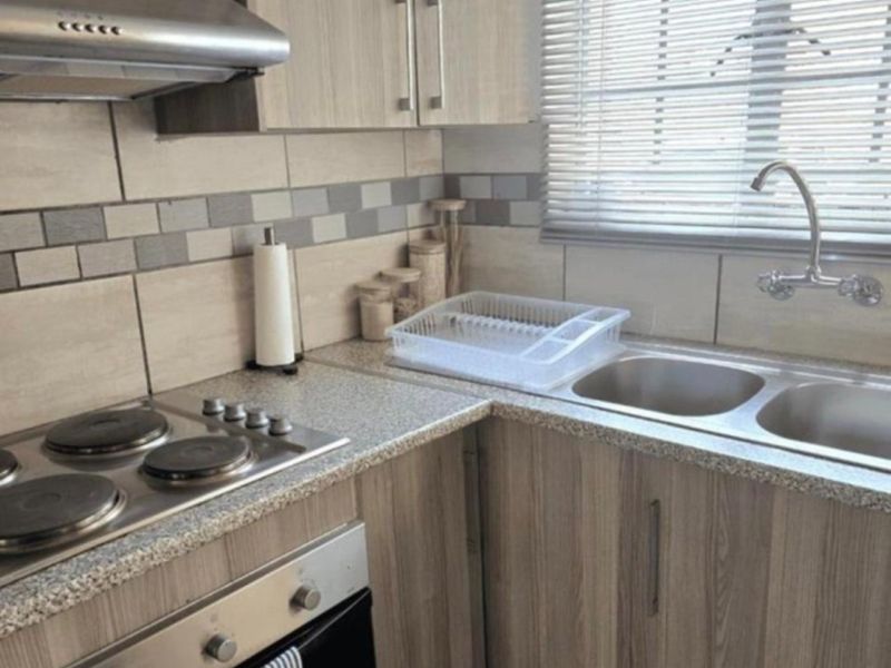 A functional kitchen featuring wood-look laminate cabinetry, stone-effect countertops, a stainless steel hob, oven, extractor fan, and a double sink with tiled splashback.