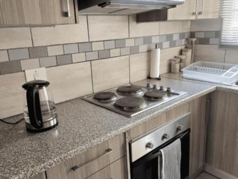 A functional kitchen featuring wood-look cabinetry, granite countertops, a built-in electric hob, oven, and a modern tiled backsplash.