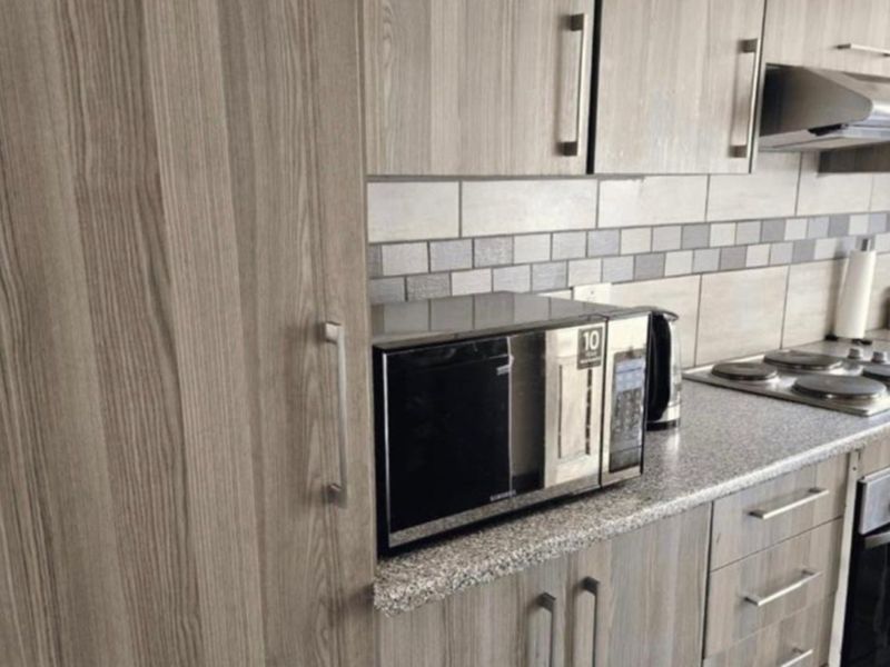Modern kitchen featuring wood-grain cabinetry, granite countertops, a tiled backsplash, and integrated appliances including an electric hob and extractor fan.