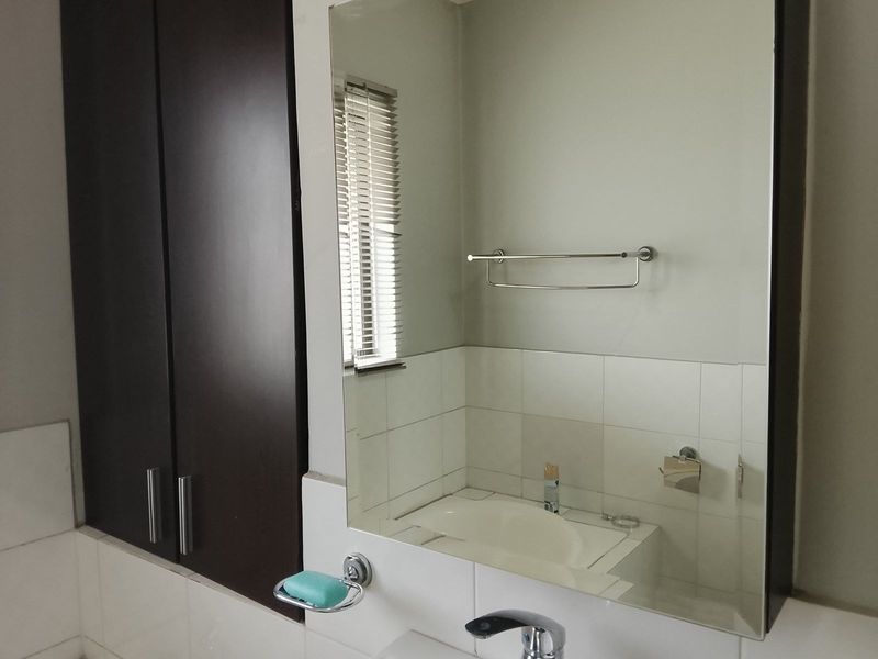 A clean bathroom featuring a built-in vanity cupboard, large wall-mounted mirror, and functional chrome fixtures including a towel rail and soap dish.